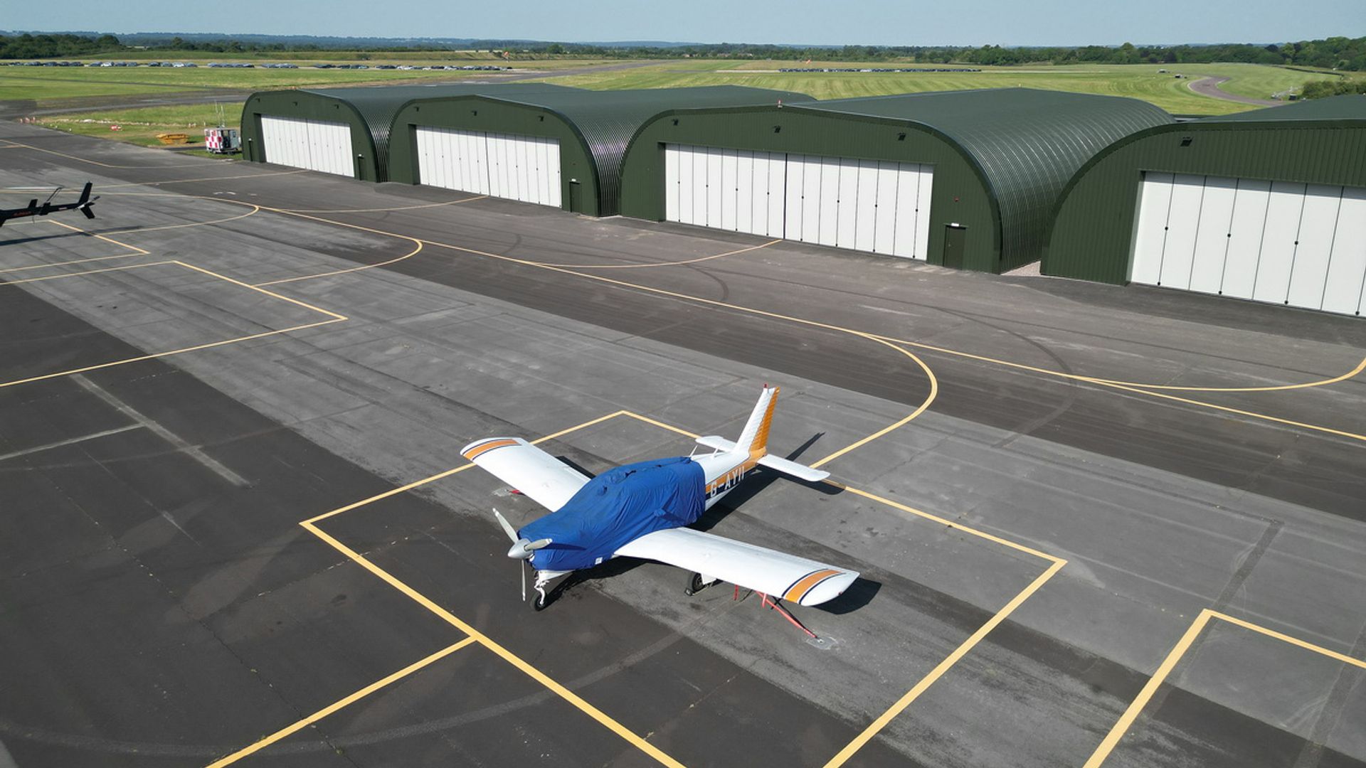 Light aircraft parked on the apron at Thruxton Airfield, with hangars behind